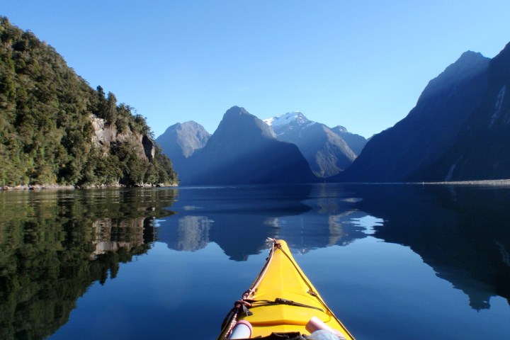 a small boat in a body of water with Milford Sound in the background